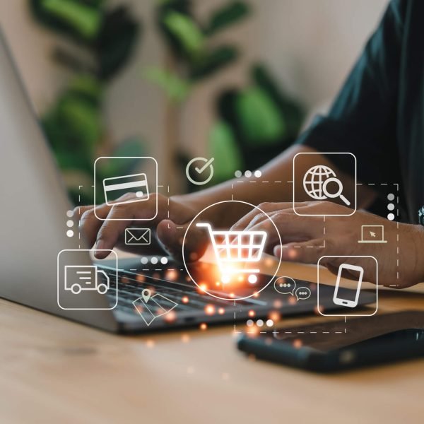 Une personne qui travaille sur un ordinateur portable et au premier il y a des icones de caddie, carte bleue, camion de livraison et un téléphone portable pour symbolisé le e-commerce